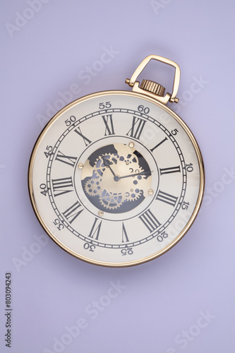 Big wall clock in the form of an antique pocket watch on a lavender background. Top view