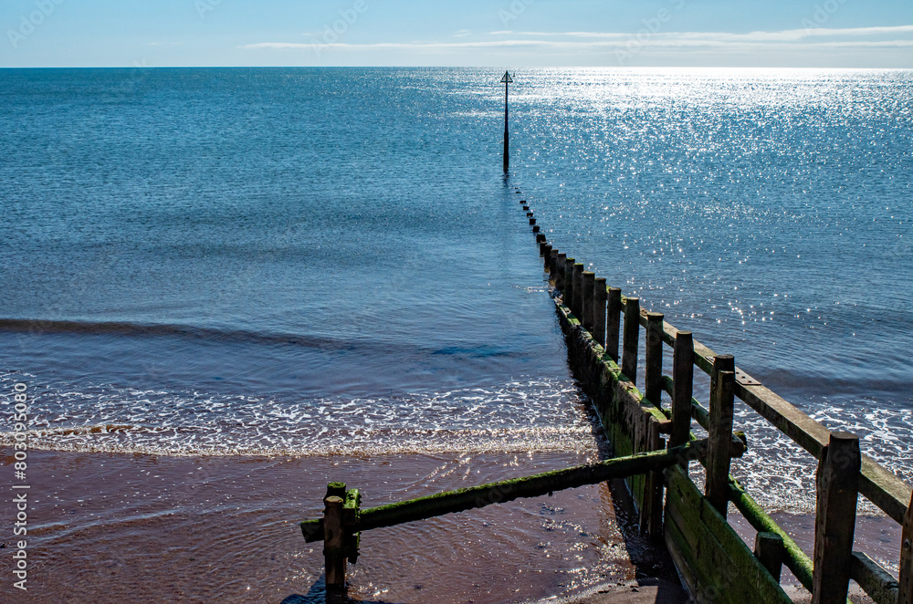 Beach sand groyne leading out to the ocean, water on a sunny day. blue sky. Calm, reflective and uplifting capture. Copy space.