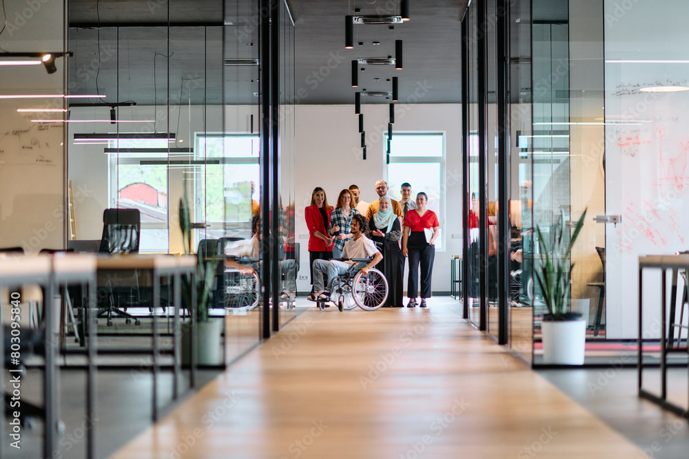 Fototapeta premium A diverse group of young business people walking a corridor in the glass-enclosed office of a modern startup, including a person in a wheelchair and a woman wearing a hijab