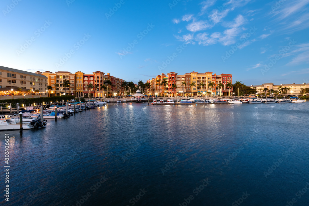 Twilight settles on Naples with waterfront buildings and boats under a clear sky.