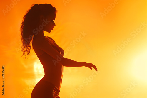 Silhouette of a female dancer rehearsing her routine on stage against warm backdrop photo