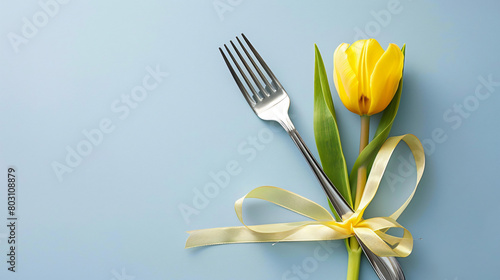 Fork with ribbon and yellow tulip on color background