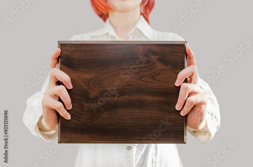 young woman holds wooden award plaque in her hands in front of her