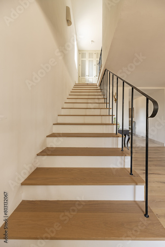 Staircase with oak wood steps of a single-family home with black minimalist style metal railing
