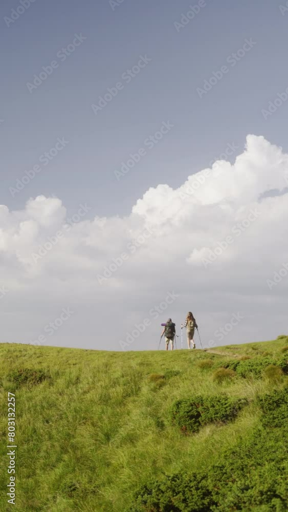 Women with backpacks and Nordic walking sticks go up hill Women with backpacks and Nordic walking sticks go up hill