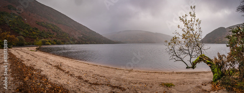 Epic panoramic view with lake, beach, trees, valley and rocky steep mountain. Bad Depressing weather. Lough Dan lake in Wicklow Mountains, Ireland