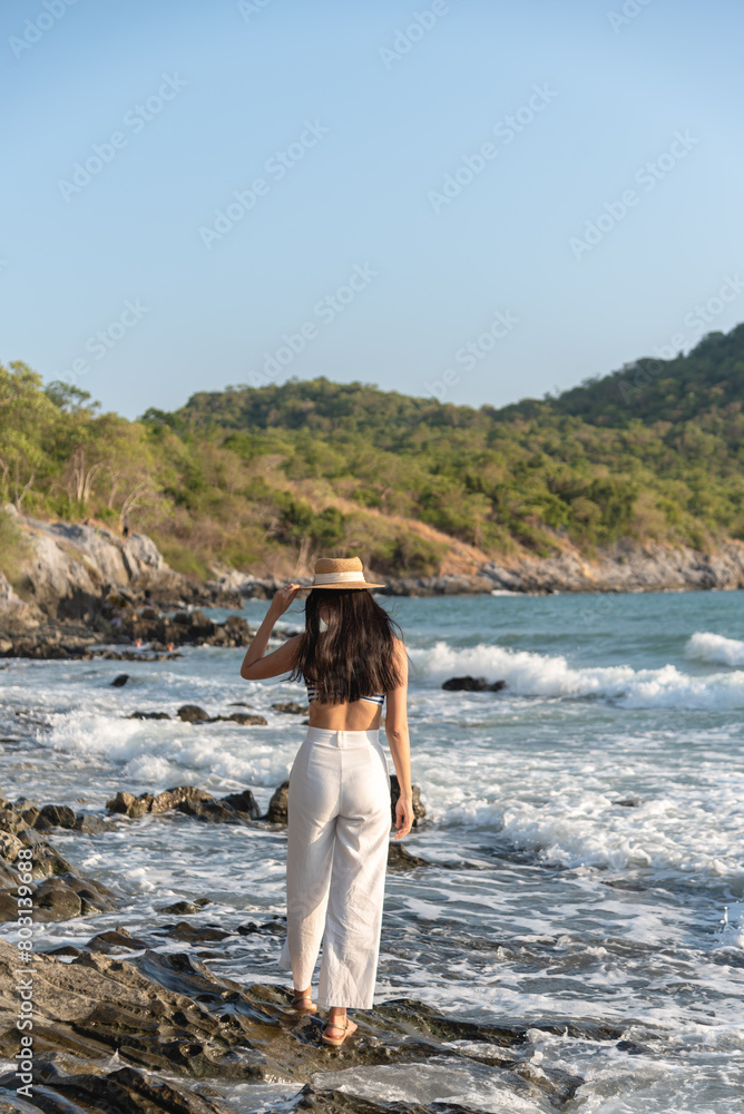 Lonely woman walk on the rock beach among wave of sea and sunshine to relax on vacation