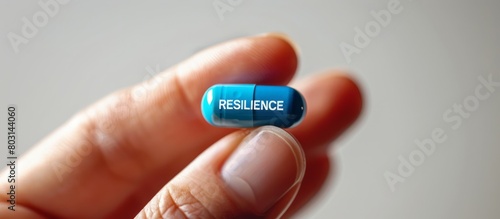 Fingers holding a blue mini pill with text RESILIENCE