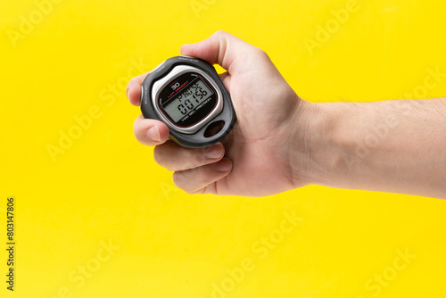 Man hand holding stopwatch on yellow background, closeup. Time management concept.