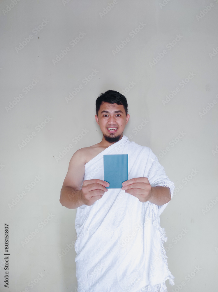 Muslim man wearing ihram cloth happy expression while holding passport Muslim man wearing ihram cloth happy expression while holding passport