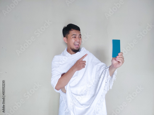 Muslim man wearing ihram cloth showing happy expression while pointing at passport photo