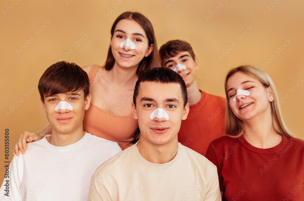 A group of cheerful teenagers with cleansing strips on their noses to remove black dots. Boys and girls take care of their facial skin. Young people do cosmetic procedures. A group of cheerful teenagers with cleansing strips on their noses to remove black dots. Boys and girls take care of their facial skin. Young people do cosmetic procedures.
