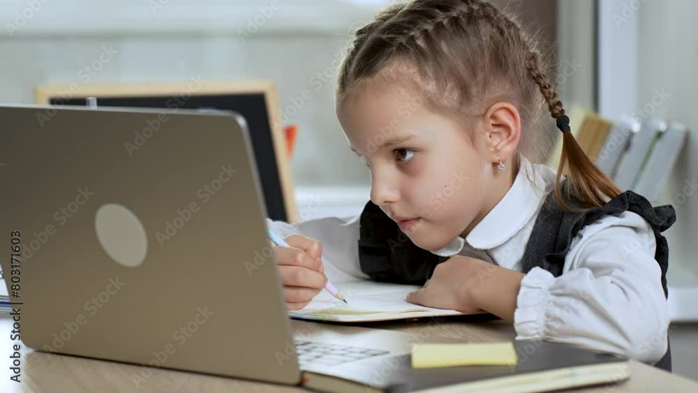 Little girl using laptop while writing notes, during online school at home Little girl using laptop while writing notes, during online school at home