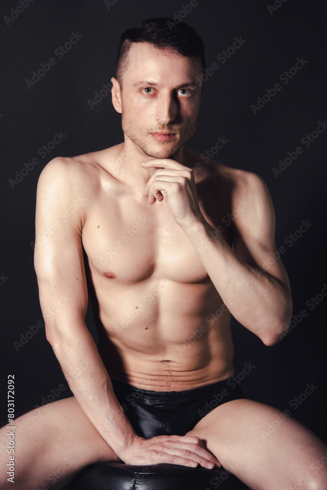 A man with a beautiful body poses in the studio against a black background.