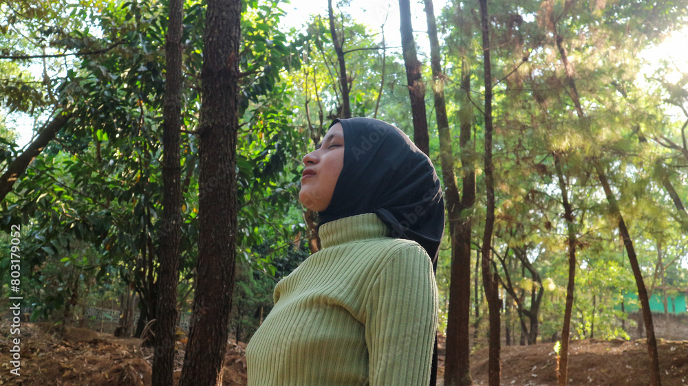 Fototapeta premium Happiness concept. Arab Woman eyes closed and breathing fresh air at pine forest with sunlight.