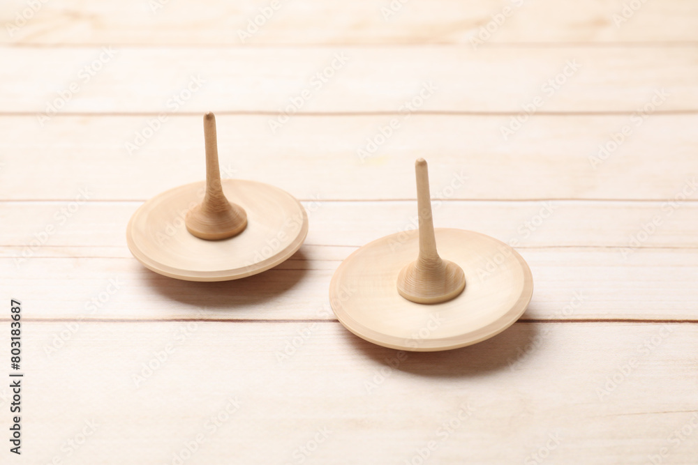 Two spinning tops on light wooden table, closeup Two spinning tops on light wooden table, closeup