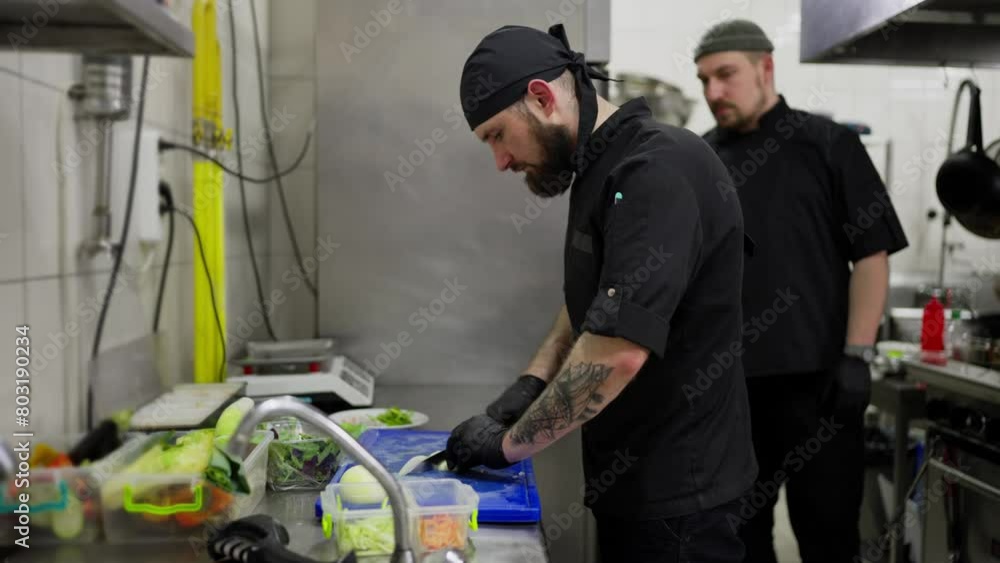 A professional male chef in a black uniform chops onions and other vegetables while starting to prepare a restaurant for work. Chefs work in the kitchen cutting vegetables and preparing dishes A professional male chef in a black uniform chops onions and other vegetables while starting to prepare a restaurant for work. Chefs work in the kitchen cutting vegetables and preparing dishes