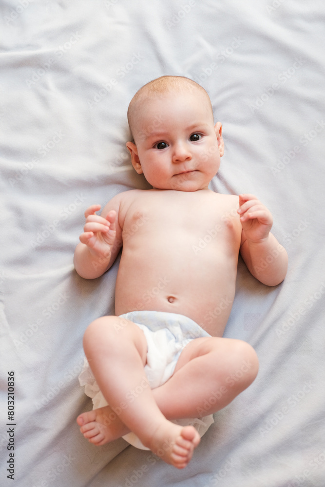 Portrait of a 4 month old Caucasian infant baby lying on a light blanket naked in a diaper and looking up. A little girl looks around in surprise, the emotions of a newborn. Mothers Day. Portrait of a 4 month old Caucasian infant baby lying on a light blanket naked in a diaper and looking up. A little girl looks around in surprise, the emotions of a newborn. Mothers Day.