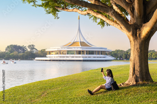 Beautiful woman using smart phone and resting at Suan Luang Rama IX Park. People enjoy and relax at Suan Luang Rama IX park summer time in Bangkok, Thailand photo