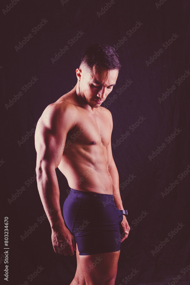 Confident, attractive shirtless muscular young man topless in studio