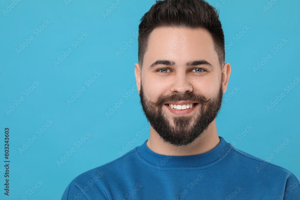 Obraz premium Portrait of happy young man with mustache on light blue background. Space for text