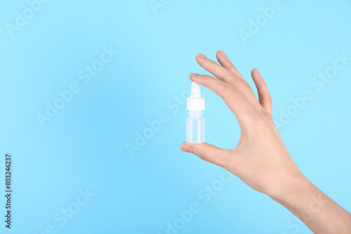 Woman with bottle of medical drops on light blue background, closeup