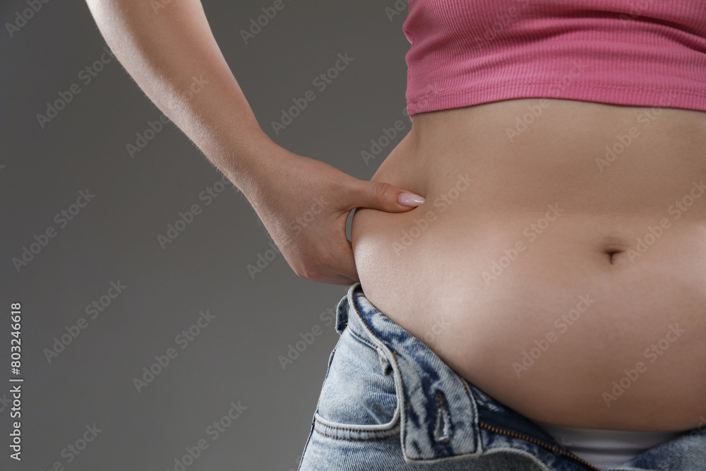 Naklejka premium Woman touching belly fat on grey background, closeup. Overweight problem