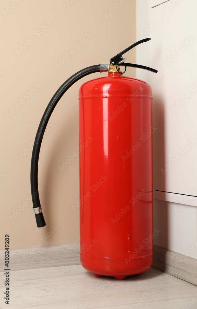 Fire extinguisher on floor near beige wall indoors
