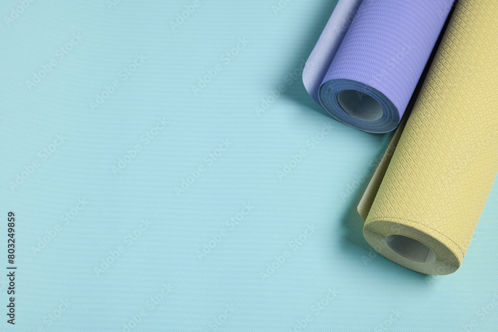 Colorful wallpaper rolls on light blue background, above view. Space for text Colorful wallpaper rolls on light blue background, above view. Space for text