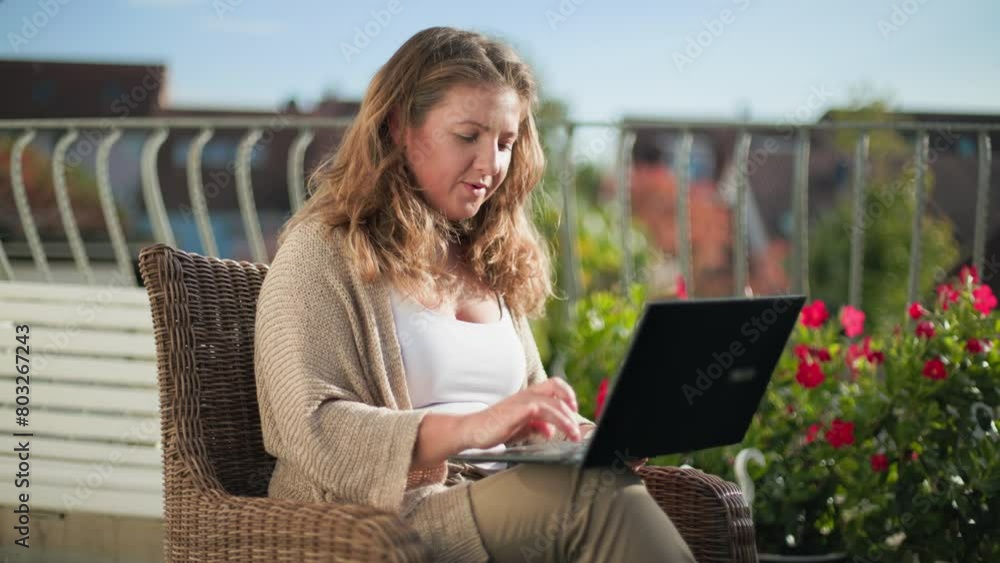 beautiful young woman working at a laptop while sitting in a chair on a loggia in open air beautiful young woman working at a laptop while sitting in a chair on a loggia in open air