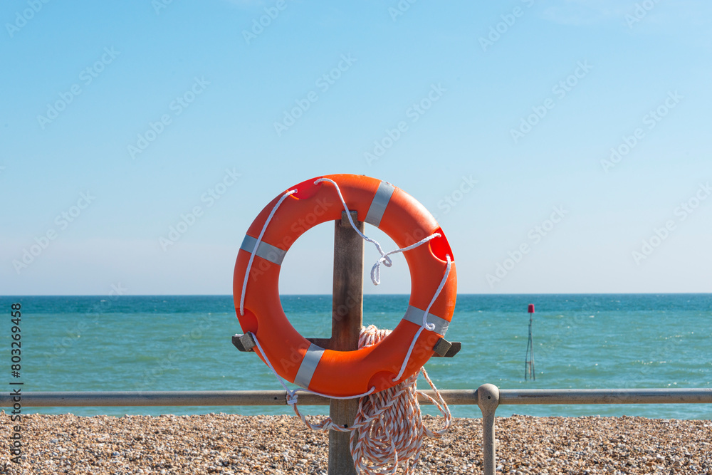 lifebouy, orange lifebouy by a beach and sea with blue sky