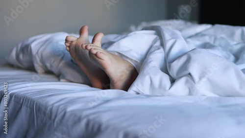 A close-up of the legs of a sleeping small child on a large white bed, embodying the concept of sleep and rest