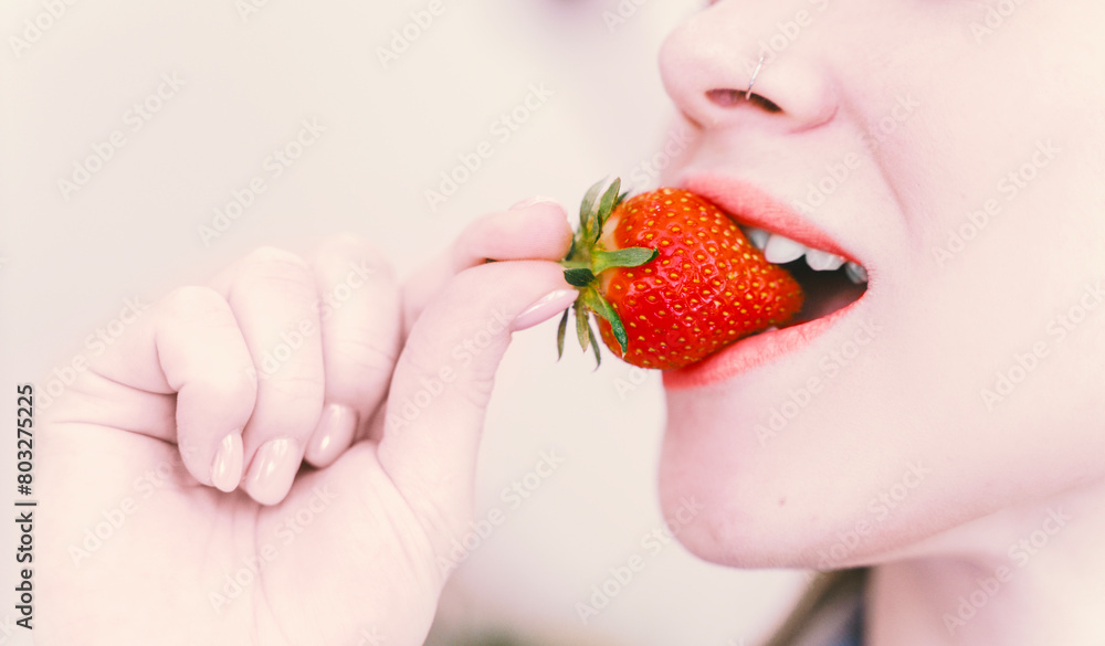 Obraz premium Beautiful girl holding ripe red strawberries in her mouth. Close-up. Selected Focus