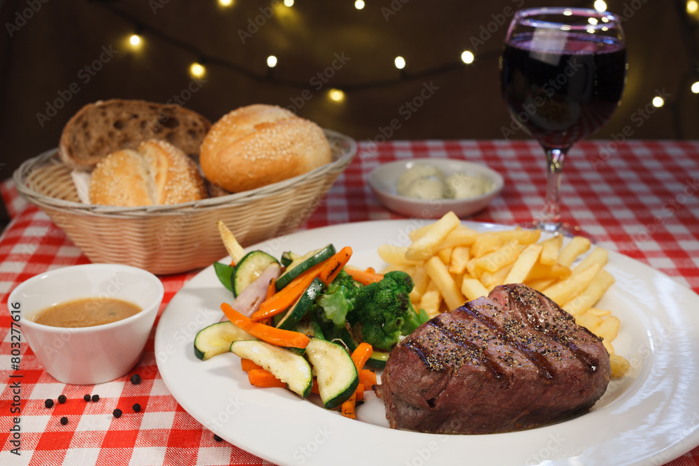 Restaurant grilled piece of steak sprinkled with pepper, french fries and vegetables, grapes and bread Restaurant grilled piece of steak sprinkled with pepper, french fries and vegetables, grapes and bread