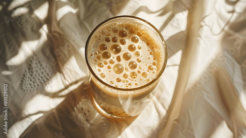 Iced coffee latte with milk foam and bubbles, cappuccino, mocha in a transparent glass glass, on a white table with sun rays from the window, close-up, top view in the corner photo