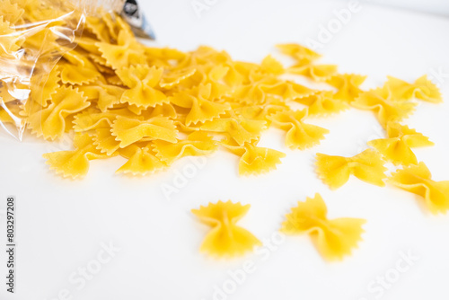Heap of dry eggless farfalle pasta isolated on a white background. Closeup of spilled yellow bow-tie pastas pile from wheat semolina. Butterfly shaped meal with saccharides, starch and gluten content.