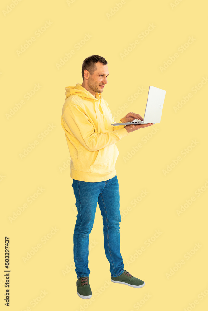 Young Caucasian man wear yellow hoodie and jeans using laptop touch screen. Full body isolated on yellow background.