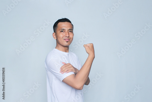 Young asian man in white t-shirt raising his right arm shows a passionate expression.