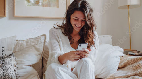 jeune fille joyeuse assise dans son canapé en train lire ses messages sur son smartphone photo