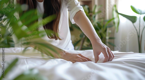 Close up of a woman making a bed with white linen sheets