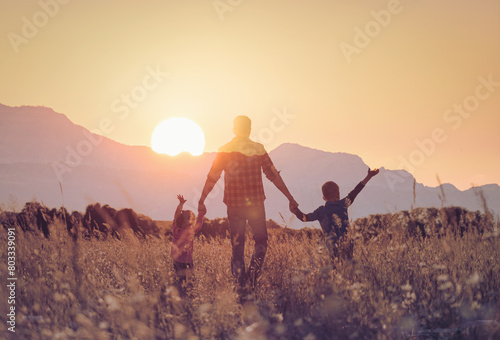 Father and his children holding hands walking in a field at sunset enjoying time together in nature © kieferpix