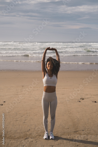 Fit black woman doing relaxation and breathing exercise at the beach. Fitness and yoga relax outdoor. Stretching arms.