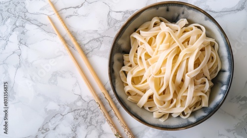 Dried udon nudles in a bowl closeup. Bunch of raw japanese vegan pasta from wheat flour and bamboo chopsticks over bowl against marble countertop. photo