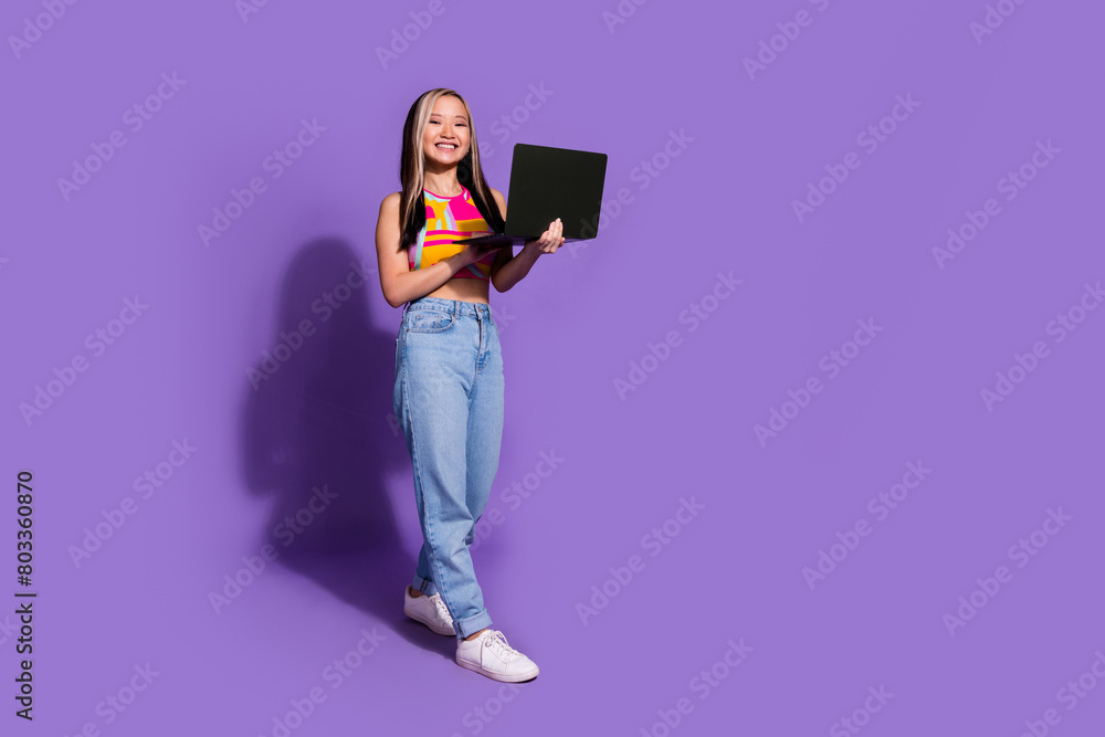 Full length photo of lovely girl wear trendy clothes advertise modern device empty space isolated on purple color background Full length photo of lovely girl wear trendy clothes advertise modern device empty space isolated on purple color background