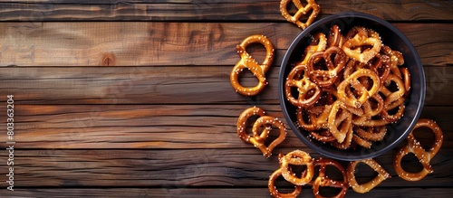 Crispy salted snacks, such as pretzels, are arranged in a dark bowl on a wooden surface, ideal for a party. Adequate space for text available.