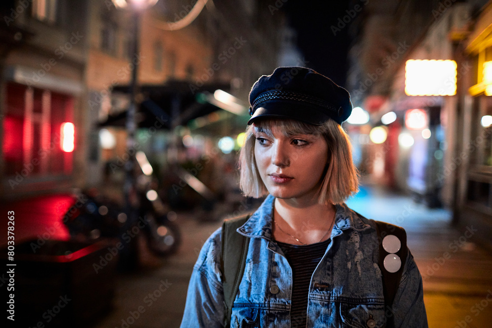 Young woman in urban night setting wearing denim jacket and cap Young woman in urban night setting wearing denim jacket and cap