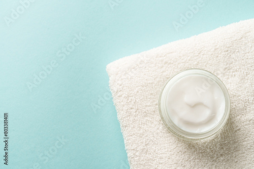 Cream jar and white towel on blue background. Skin care product. Flat lay image.