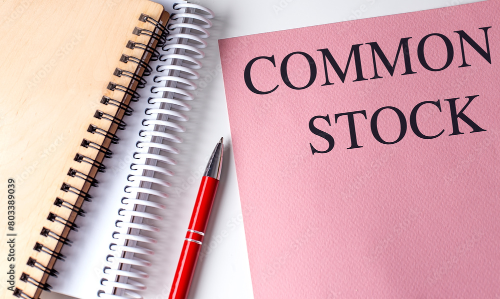 COMMON STOCK text on pink paper with notebooks COMMON STOCK text on pink paper with notebooks