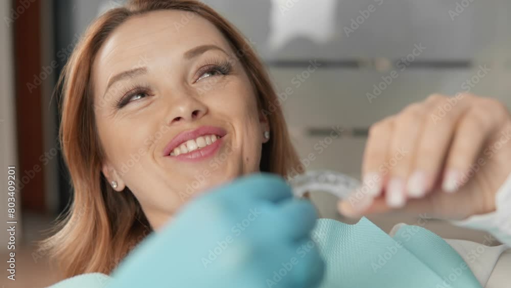 The patient looks at the mouth guard veneers shown by the doctor, expressing interest in the possibility of improving her smile. The doctor talks about the procedure for their installation and result. The patient looks at the mouth guard veneers shown by the doctor, expressing interest in the possibility of improving her smile. The doctor talks about the procedure for their installation and result.