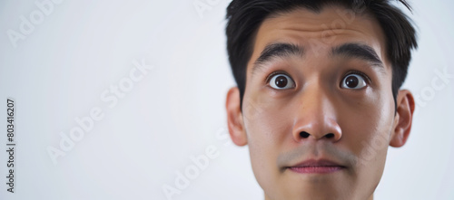 Close-up of a young man with a surprised expression, large eyes, and raised eyebrows isolated on a white background with ample copy space on the left photo